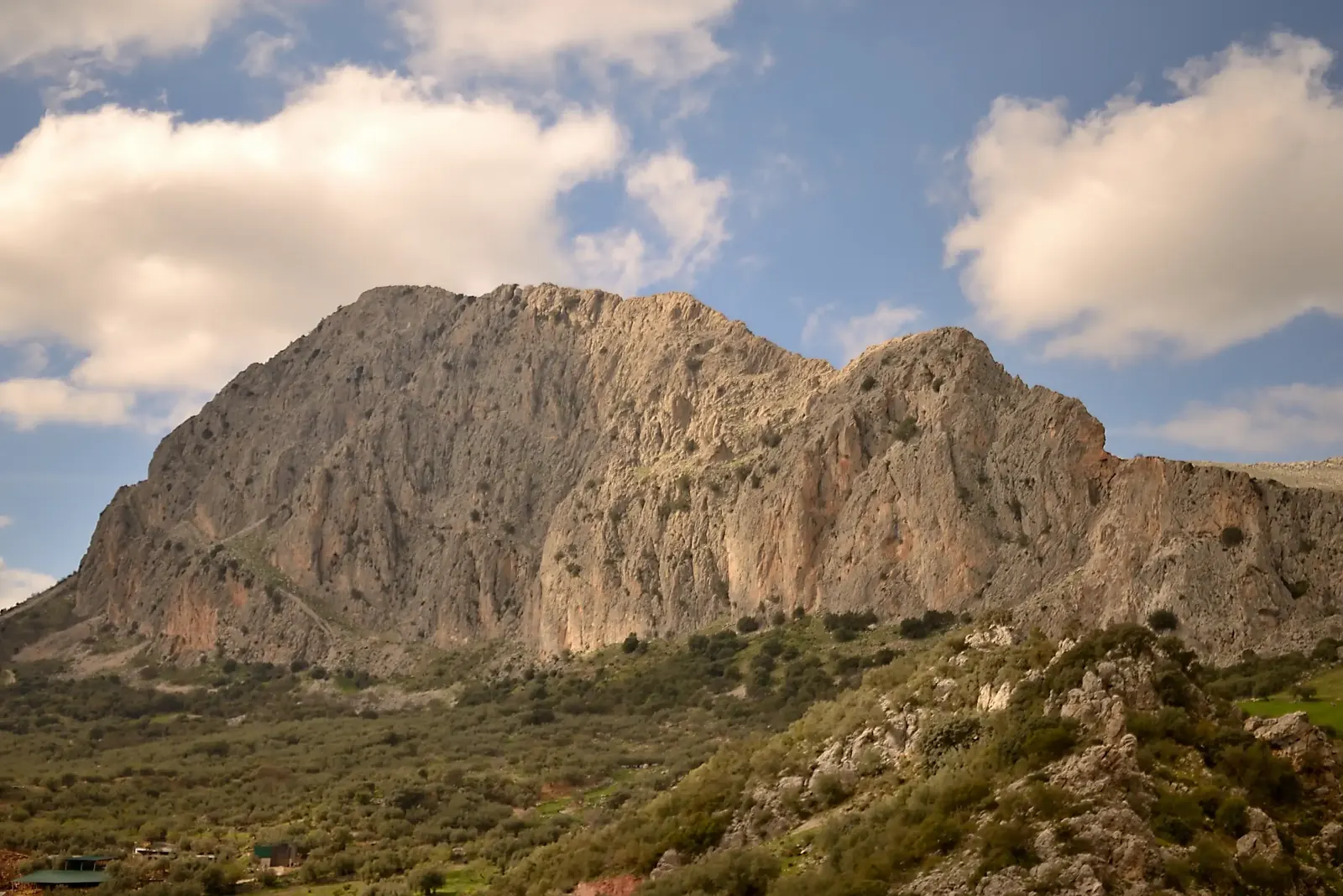 A sunlit limestone massif rising above green hills under a wide sky